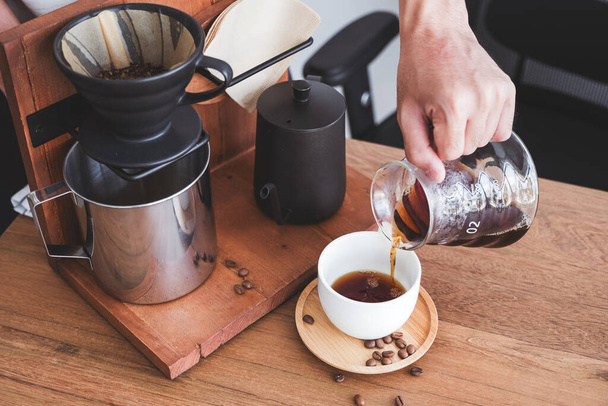 Closeup image of a hand pouring drip coffee into a white mug on vintage wooden table - Foto, imagen