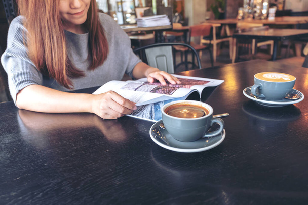 Imagen de cerca de una hermosa mujer asiática leyendo revista con taza de café en la mesa en la cafetería moderna
  - Foto, Imagen