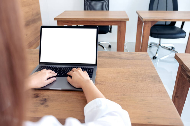 Mockup obrázek ženy pomocí a psaní na notebook s prázdnou bílou desktopovou obrazovkou na dřevěném stole v kanceláři - Fotografie, Obrázek