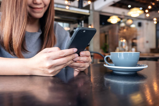 Imagen de cerca de una mujer sosteniendo y usando un teléfono inteligente con taza de café en la mesa
 - Foto, Imagen