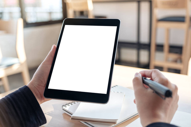 Mockup kép kezek gazdaság és használata fekete tabletta pc üres fehér asztali képernyőn, miközben írás notebookok az irodában - Fotó, kép