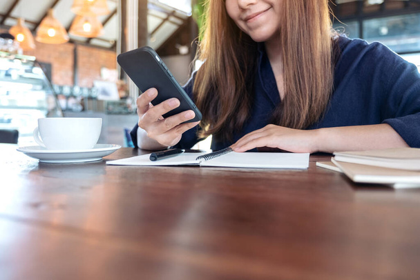 Крупним планом зображення красивої азіатки тримає, використовуючи і дивлячись на смартфон під час роботи в кафе
 - Фото, зображення