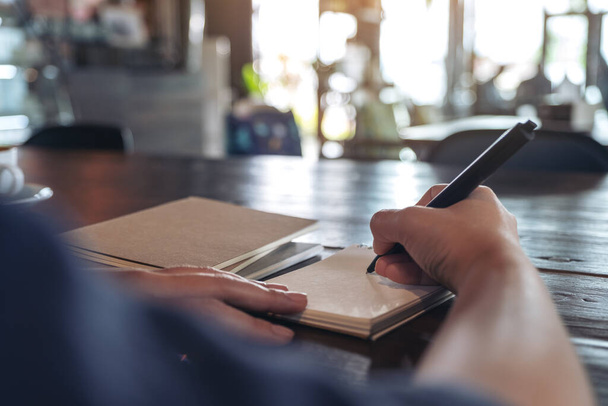 Nahaufnahme einer Frau, die auf ein leeres Notizbuch auf dem Tisch im Café schreibt - Foto, Bild