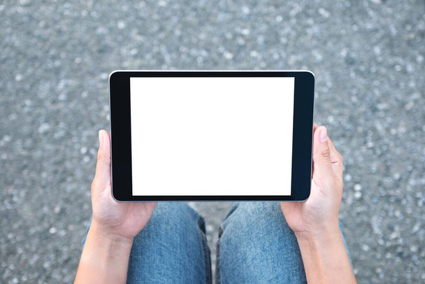 Vista dall'alto immagine mockup di una donna che tiene il tablet pc nero con schermo bianco vuoto mentre si siede sullo sfondo della strada
  - Foto, immagini