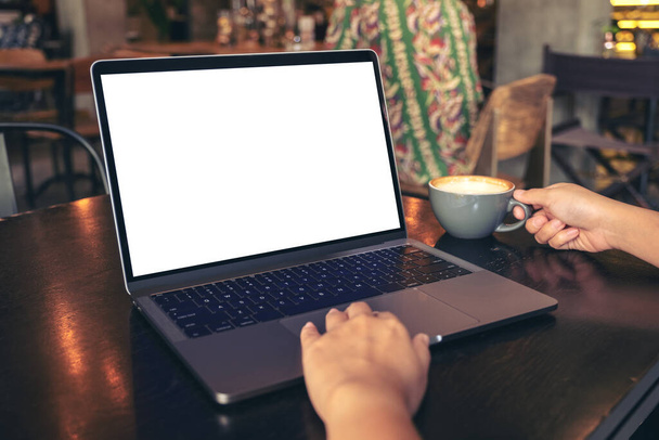 Образец женских рук с помощью ноутбука с чистым белым экраном рабочего стола во время питья горячего кофе на деревянном столе в кафе
 - Фото, изображение