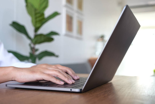 Imagem de close-up das mãos da mulher usando e digitando no teclado do laptop na mesa de madeira no escritório
 - Foto, Imagem