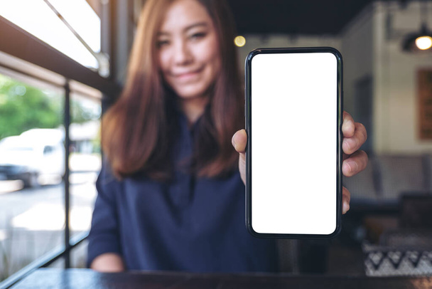Mockup obraz asijské podnikatelky držení a zobrazení černého mobilního telefonu s prázdnou bílou obrazovkou v kavárně - Fotografie, Obrázek