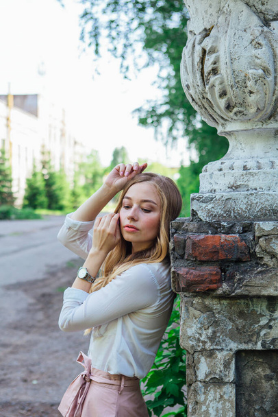 Portrait of a beautiful blond girl standing next to an old building with a decorative antique vase and stairs - 写真・画像