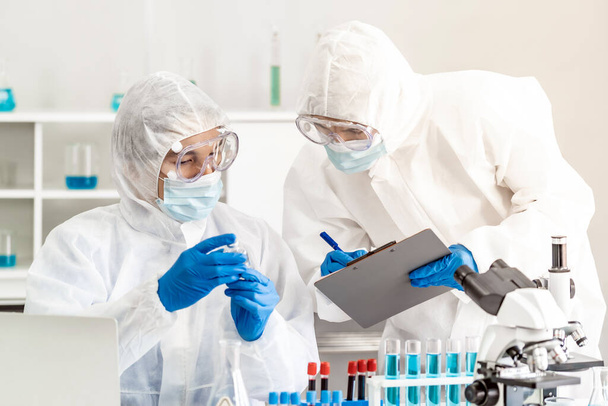 Scientist examine vaccine testing of coronavirus covid-19 pandemic in science lab. Scientist wear PPE personal protective suits and medical goggles. Medical Science technology and healthcare concept. - Photo, Image