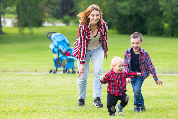 Sevimli, neşeli iki erkek kardeş, annesiyle birlikte parkta oynuyorlar. Aile hayatının mutluluğu ve ahengi. Harika bir aile tatili.  - Fotoğraf, Görsel