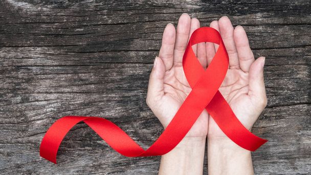 Světový den pomůcek a národní měsíc povědomí o HIV / AIDS a stárnutí s červenou stuhou na ženské podpoře rukou (luk izolovaný s výstřižkem) - Fotografie, Obrázek