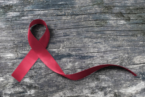 Бургундская лента для множественной миеломы MM рака и серповидноклеточной анемии осведомленности на старом деревянном фоне - Фото, изображение