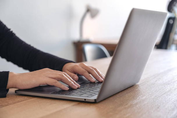 Imagem de close-up de mãos usando e digitando no teclado do laptop na mesa de madeira no escritório
 - Foto, Imagem