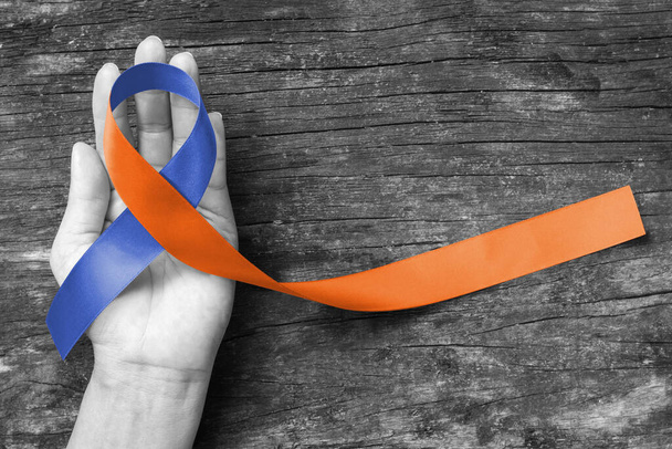 Derechos humanos para los cuidadores familiares conciencia en color azul marino naranja cinta de tela salpicada en fondo envejecido mano humana - Foto, Imagen