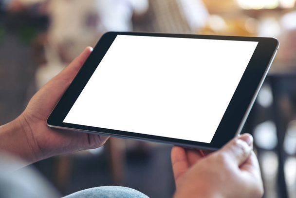 Imagen burlona de una mujer sosteniendo PC tableta negra con pantalla blanca en blanco horizontalmente mientras está sentado en la cafetería - Foto, Imagen