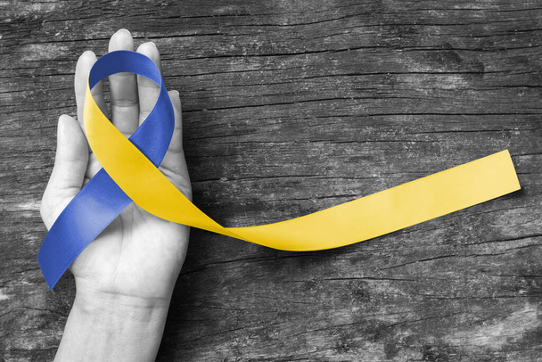 Blue yellow awareness ribbon on helping hand for World down syndrome day WDSD March 21 raising support on patient with down syndrome illness disability and Thoracic Outlet Syndrome - (TOS) - Photo, Image