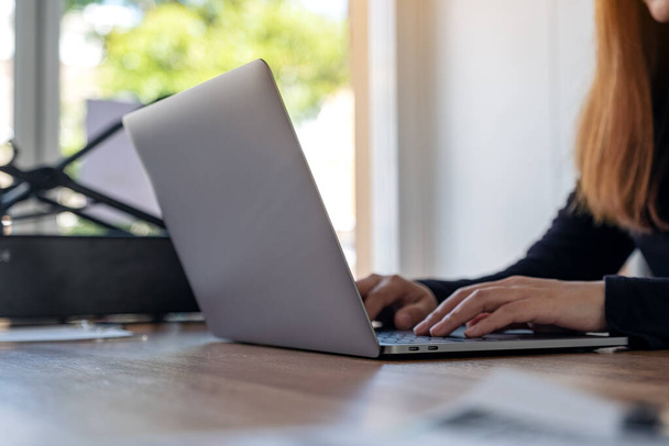 Imagem de close-up de uma mulher usando e digitando no teclado do laptop na mesa de madeira no escritório
 - Foto, Imagem