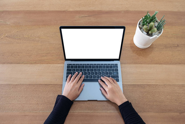 Imagem de maquete de vista superior de uma mulher usando e digitando no laptop com tela branca em branco e pote de cacto no fundo da mesa de madeira
  - Foto, Imagem