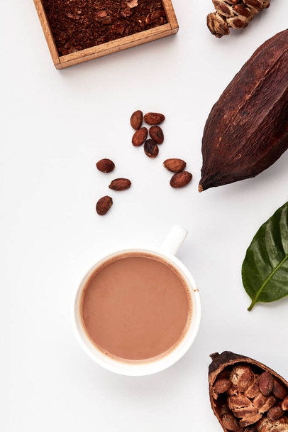 Becher Kakao Heißgetränk mit Kakaoschoten, Kakaopulver, Kakaobohnen, auf weißem Hintergrund, flaches Lay-Food-Konzept - Foto, Bild