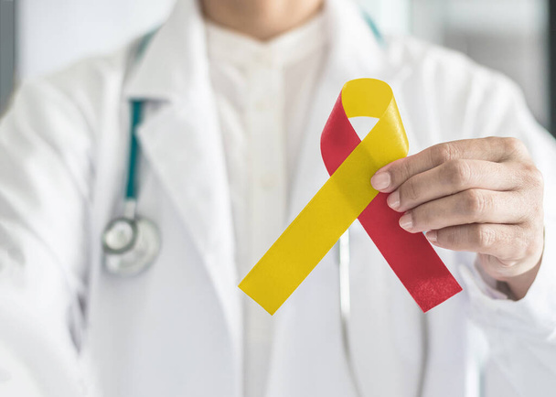 World hepatitis day and HIV/ HCV co-infection awareness with red yellow ribbon in medical doctor hand symbolic bow color to support patient with illness and hepatic disease - Fotó, kép