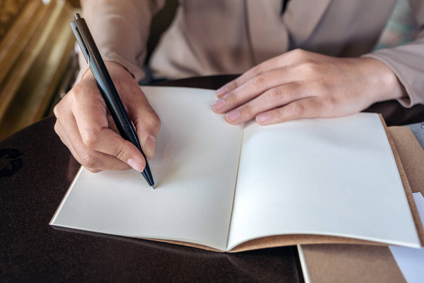 Imagen de primer plano de una mujer de negocios escribiendo en cuaderno en blanco en una mesa de madera
 - Foto, imagen