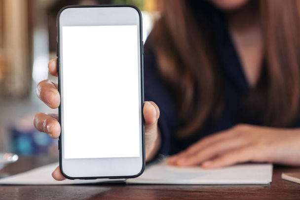 Изображение женщины, держащей и показывающей белый мобильный телефон с пустым экраном в кафе
 - Фото, изображение