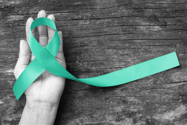 Mint green ribbon awareness for Genetic Disorder, Ivemark Syndrome, Congenital hepatic Fibrosis, and Autosomal Recessive Polycystic Kidney Disease with bow on helping hand support on aged wood - Photo, Image