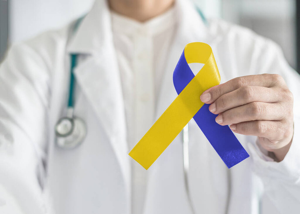 Día del síndrome de Down azul amarilla cinta de conciencia en la mano del médico para aumentar el apoyo en el paciente con síndrome de Down discapacidad enfermedad y síndrome de Outlet torácico - (TOS) - Foto, imagen