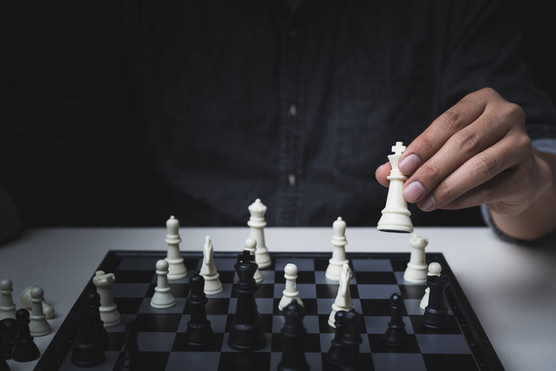 Z bliska widok dłoni mężczyzny w białej szachownicy w czarnej koszuli na czarnym tle, koncepcja konkurencji biznesowej - Zdjęcie, obraz