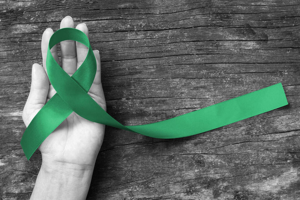 Liver Cancer Awareness κορδέλα Emerald Πράσινο χρώμα κορδέλα σε ανθρώπινο χέρι γερασμένο φόντο, ψαλίδισμα διαδρομή: σατέν ύφασμα συμβολικό λογότυπο αυξάνοντας την υποστήριξη βοηθήσει τους ανθρώπους που ζουν με την ασθένεια του όγκου - Φωτογραφία, εικόνα