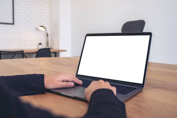 Mockup-Bild der Hände mit und Tippen auf Laptop mit leerem weißen Desktop-Bildschirm auf Holztisch im Büro - Foto, Bild