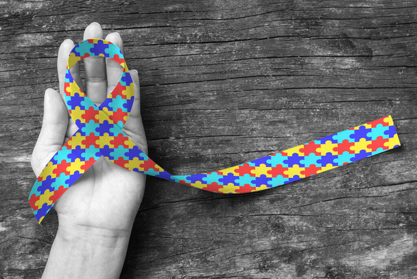 世界自閉症啓発デーWAAD:カラフルなパズル生地のリボンのロゴの色が人間の手の背景に飛び散った精神衛生疾患を持つ人々の生活に対する国民の支持運動を高める - 写真・画像