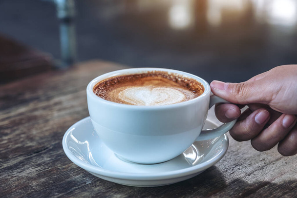 Image rapprochée d'une main tenant une tasse bleue de café chaud sur une table en bois dans un café - Photo, image