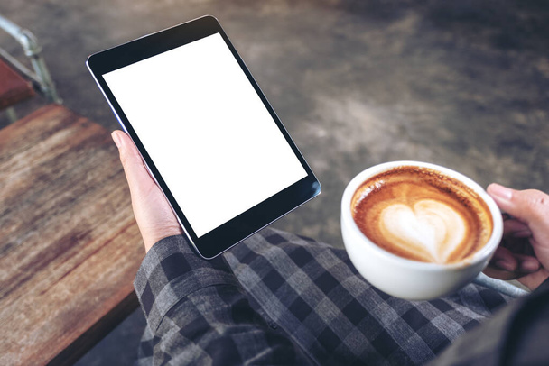 Макетне зображення рук жінки, що тримає чорний планшетний ПК з порожнім екраном під час пиття кави в кафе
 - Фото, зображення