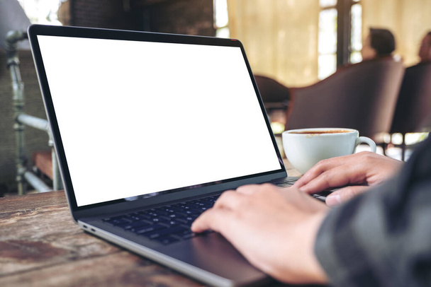 Mockup-Bild der Hände mit und Tippen auf Laptop mit leeren weißen Desktop-Bildschirm mit Kaffeetasse auf Holztisch im Café - Foto, Bild