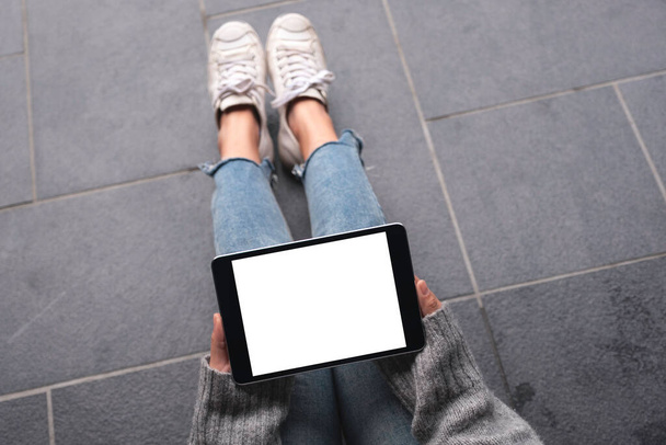 Top view mockup image of woman's hands holding and using black tablet pc with blank white desktop screen while sitting on the floor  - 写真・画像