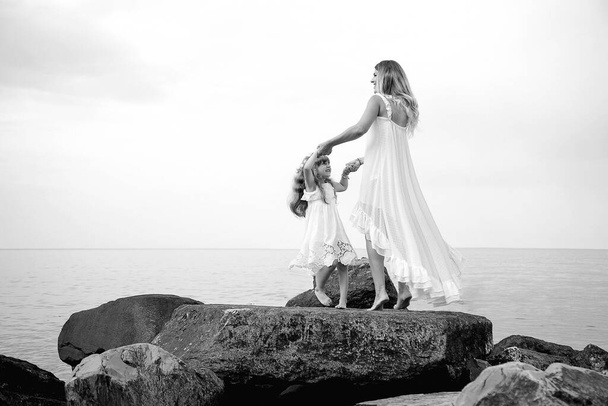 black and white photo, mother and daughter dancing on big rocks, on a wild beach near the sea - Valokuva, kuva