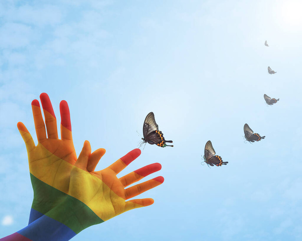 Conceito de dia de discriminação zero com padrão de bandeira do arco-íris na mão das pessoas em forma de borboleta
 - Foto, Imagem