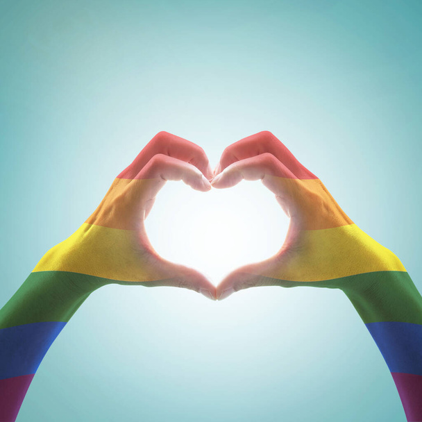 Gökkuşağı rengi bayrak deseni, mavi renkli arka planda kalp şeklinde şekillenen kadın eli: LGBT toplumunun aşk ve evlilik sosyal eşitliği ve insan kavramında sembolik eşit haklar - Fotoğraf, Görsel