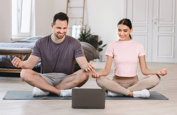 Mutlu çift dizüstü bilgisayarda oturup evde meditasyon yapıyor. - Fotoğraf, Görsel