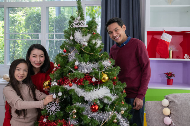 Azjatycka szczęśliwa rodzina, ojciec, matka, córka pomóc przygotować i prezent lub udekorować choinkę w salonie, który urządzony na święta Bożego Narodzenia koncepcji wakacje - Zdjęcie, obraz