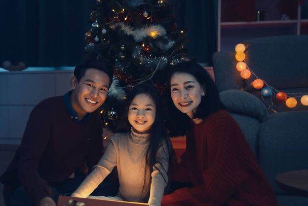 Gelukkig gezin en klein meisje open magische geschenkdoos met licht schijnt in de woonkamer die versierd met kerstboom voor Kerstmis festival binnenkort, Aziatische kerst familie concept - Foto, afbeelding