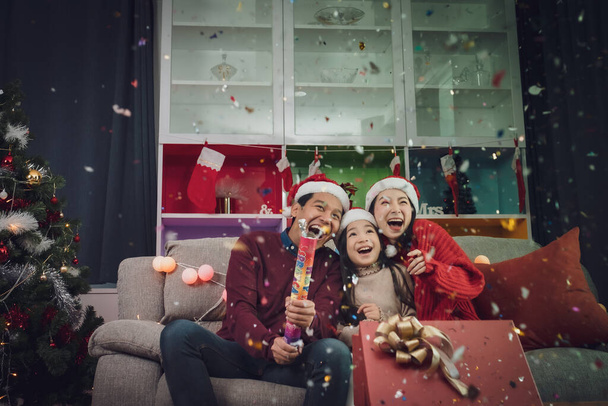 happy family man, woman, little girl play firecracker, firework to celebrate "New Year" together at christmas day night in room that decorated with christmas tree for Asian christmas festival day - Foto, Bild