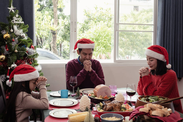 Asyalı mutlu aile Noel günü yemek yemeden önce dua eder. Mutludurlar ve birlikte yemek yerler. - Fotoğraf, Görsel