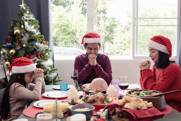 アジアの幸せな家族はクリスマスの日に食事をする前に祈る、彼らは幸せであり、一緒に食事をする - 写真・画像