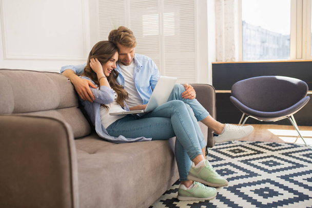 Young couple in denim sitting on a sofa watching something online and feeling comfortable - Foto, Bild
