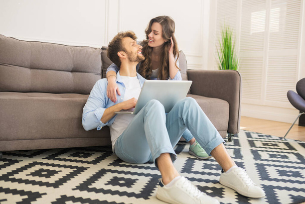 Young couple in denim sitting on a floor watching something and looking romantic - Photo, image