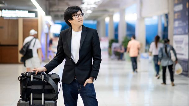 Incheckconcept voor zakenreizen en bagagevorderingen. Slimme Aziatische zakenman draagt formele pak jas dragen koffer bagage en rugzak wachten op de vlucht in de internationale luchthaven terminal. - Foto, afbeelding