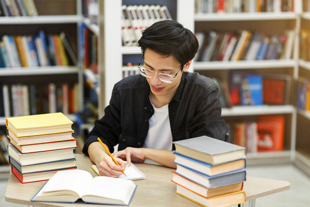 Asiatisch guy doing hometask sitting bei schreibtisch im bibliothek - Foto, Bild