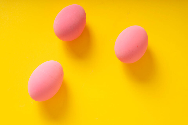 Top view - Three pink eggs over yellow background. - Foto, afbeelding